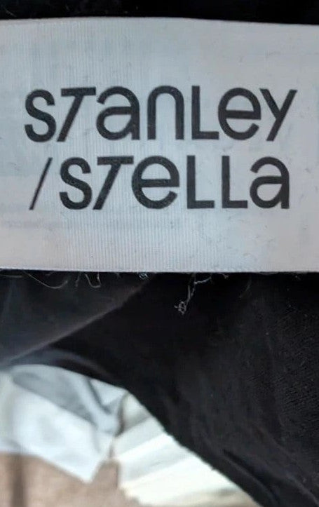 Stanley/Stella black graphic tee featuring Oasis logo and "Roll With It" beach artwork.