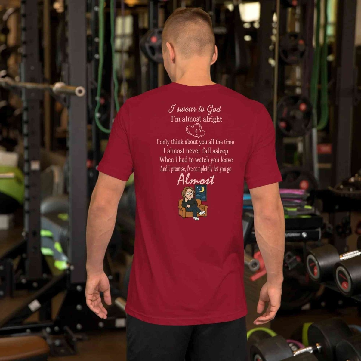 Man wearing maroon Lewis Capaldi lyrics t-shirt with text and cartoon sitting on couch in gym