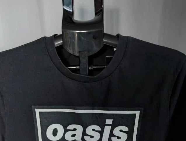 Stanley/Stella black graphic tee featuring Oasis logo and "Roll With It" beach artwork.