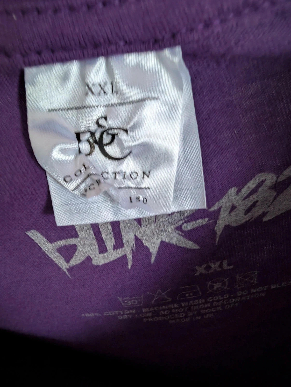 Blink-182 purple graphic tee featuring smiley face logo with neon pink outlining and drip detailing.