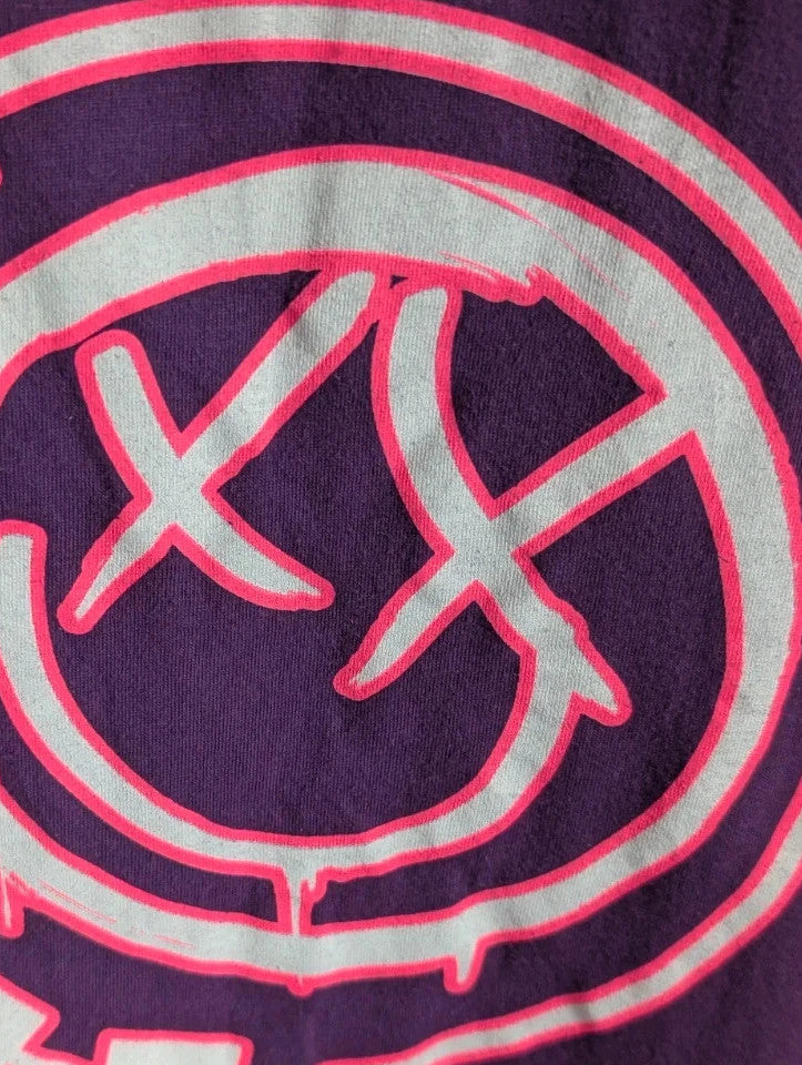Blink-182 purple graphic tee featuring smiley face logo with neon pink outlining and drip detailing.