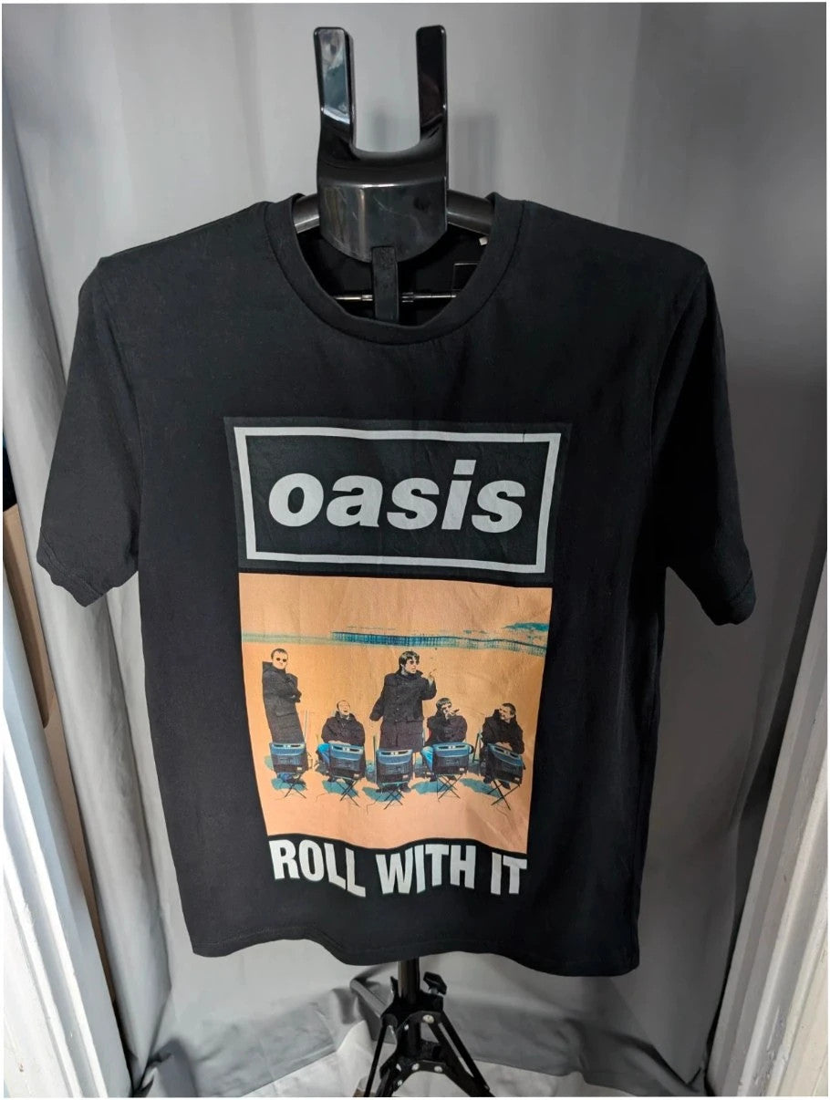 Stanley/Stella black graphic tee featuring Oasis logo and "Roll With It" beach print.