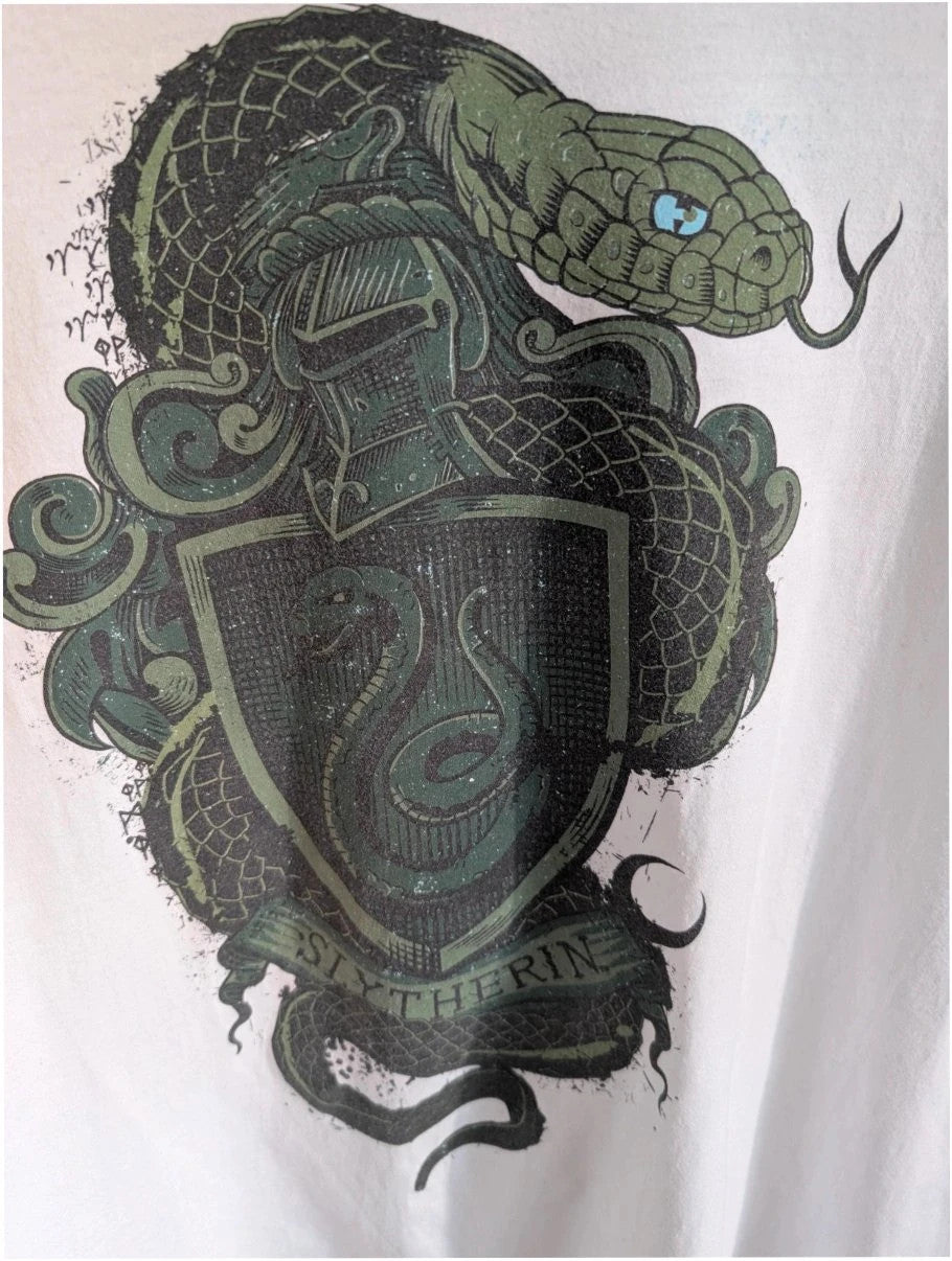 Harry Potter white graphic tee featuring green Slytherin crest and coiling snake design.
