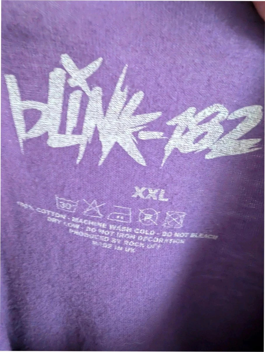 Blink-182 purple graphic t-shirt featuring smiley face logo with neon pink drip detailing.