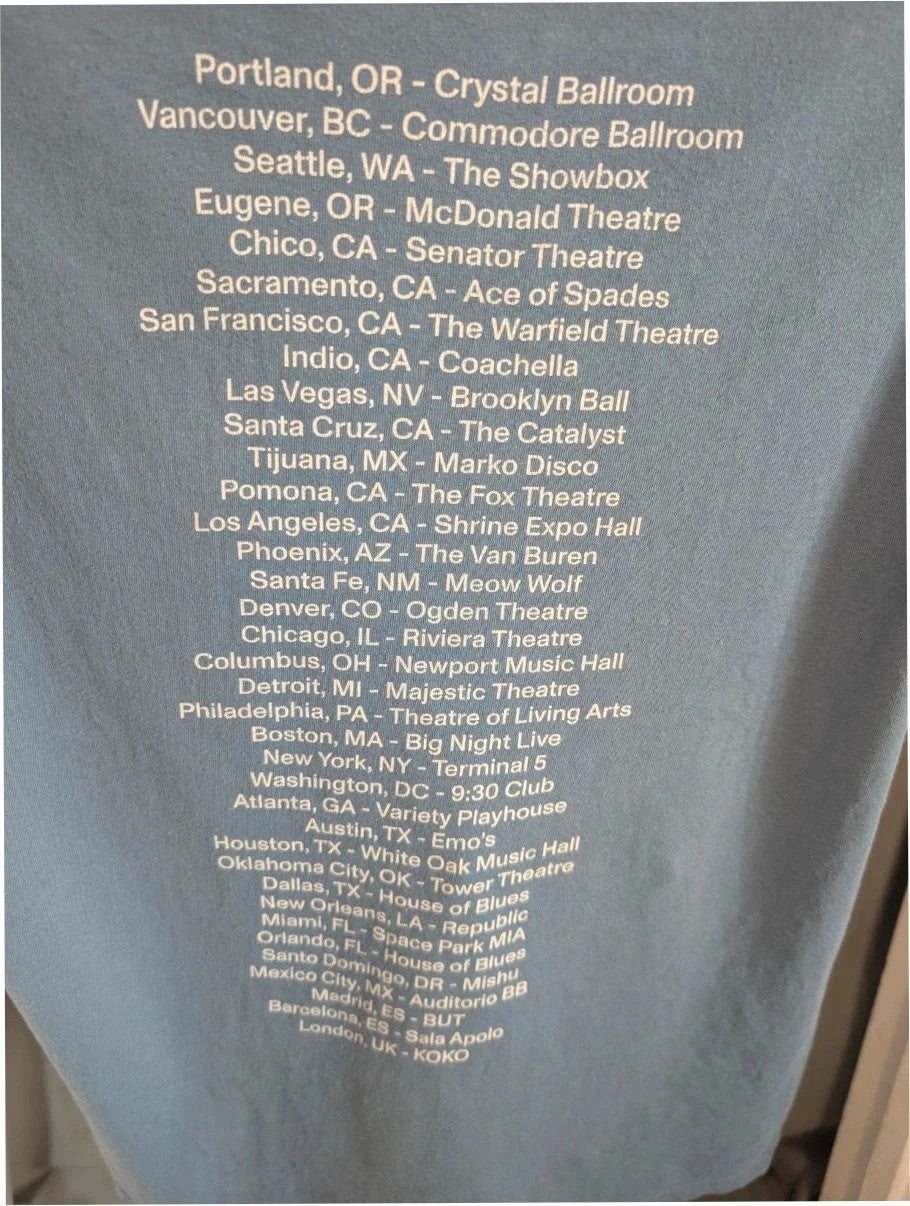 Omar Apollo blue graphic tee featuring portrait print and tour date list on back.