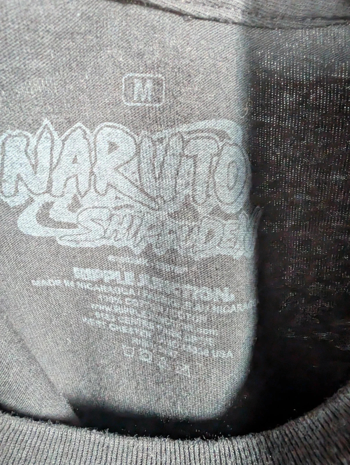 Naruto black graphic t-shirt featuring Kakashi Hatake, bubble typography, and Sharingan eye design.