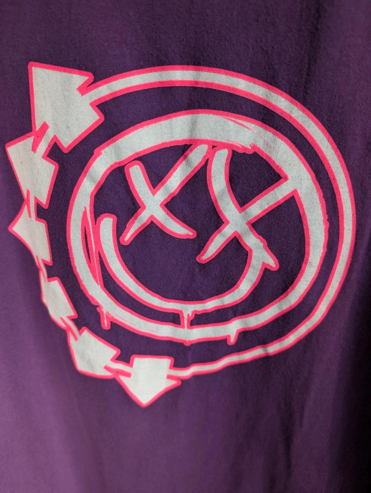 Blink-182 purple graphic tee featuring smiley face logo with neon pink outlining and drip detailing.