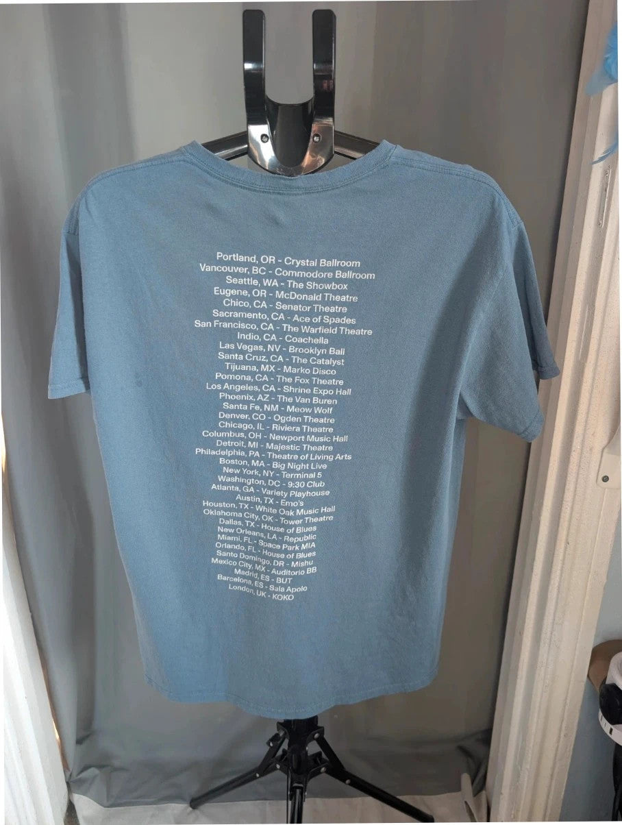 Omar Apollo blue graphic tee featuring portrait print and tour date list on back.