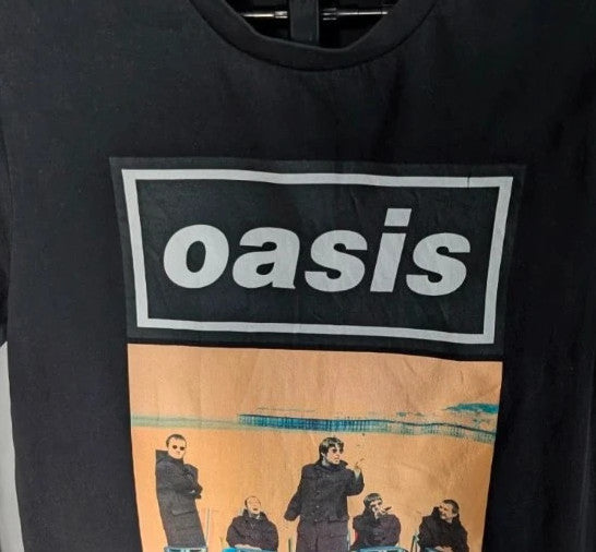 Stanley/Stella black graphic tee featuring Oasis logo and "Roll With It" beach print.