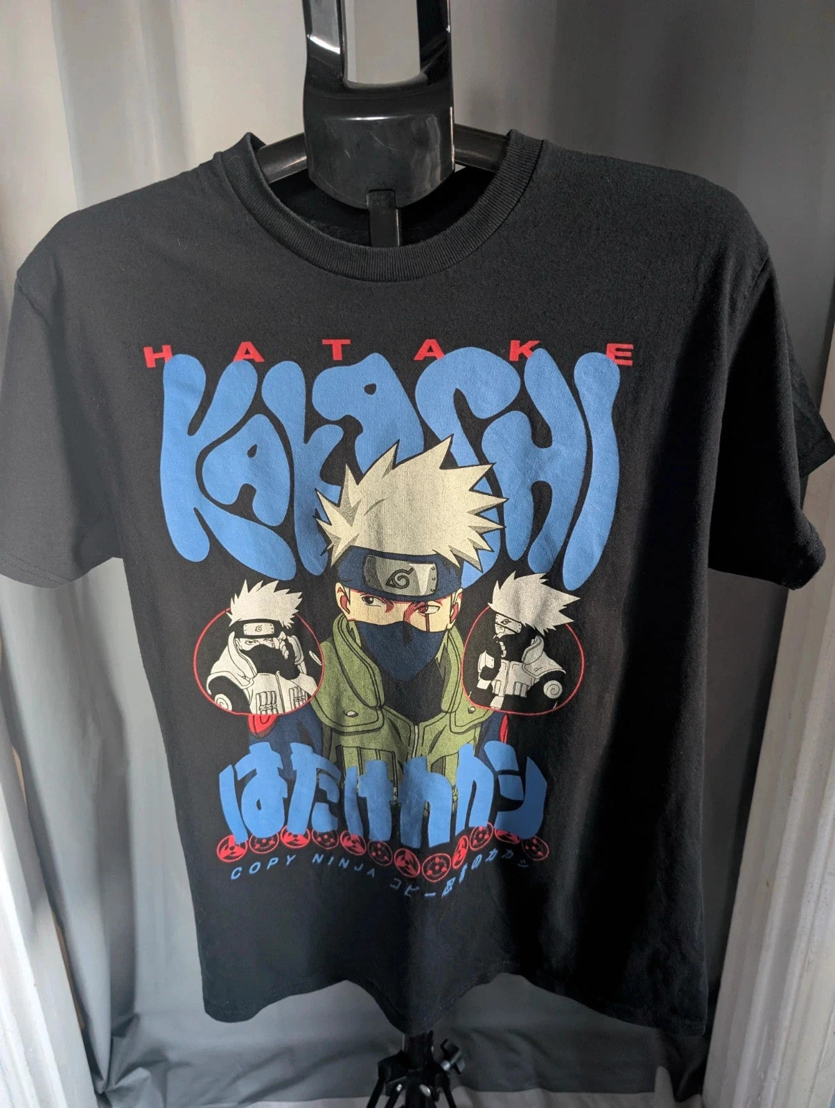 Naruto black graphic t-shirt featuring Kakashi Hatake, bubble typography, and Sharingan eye design.