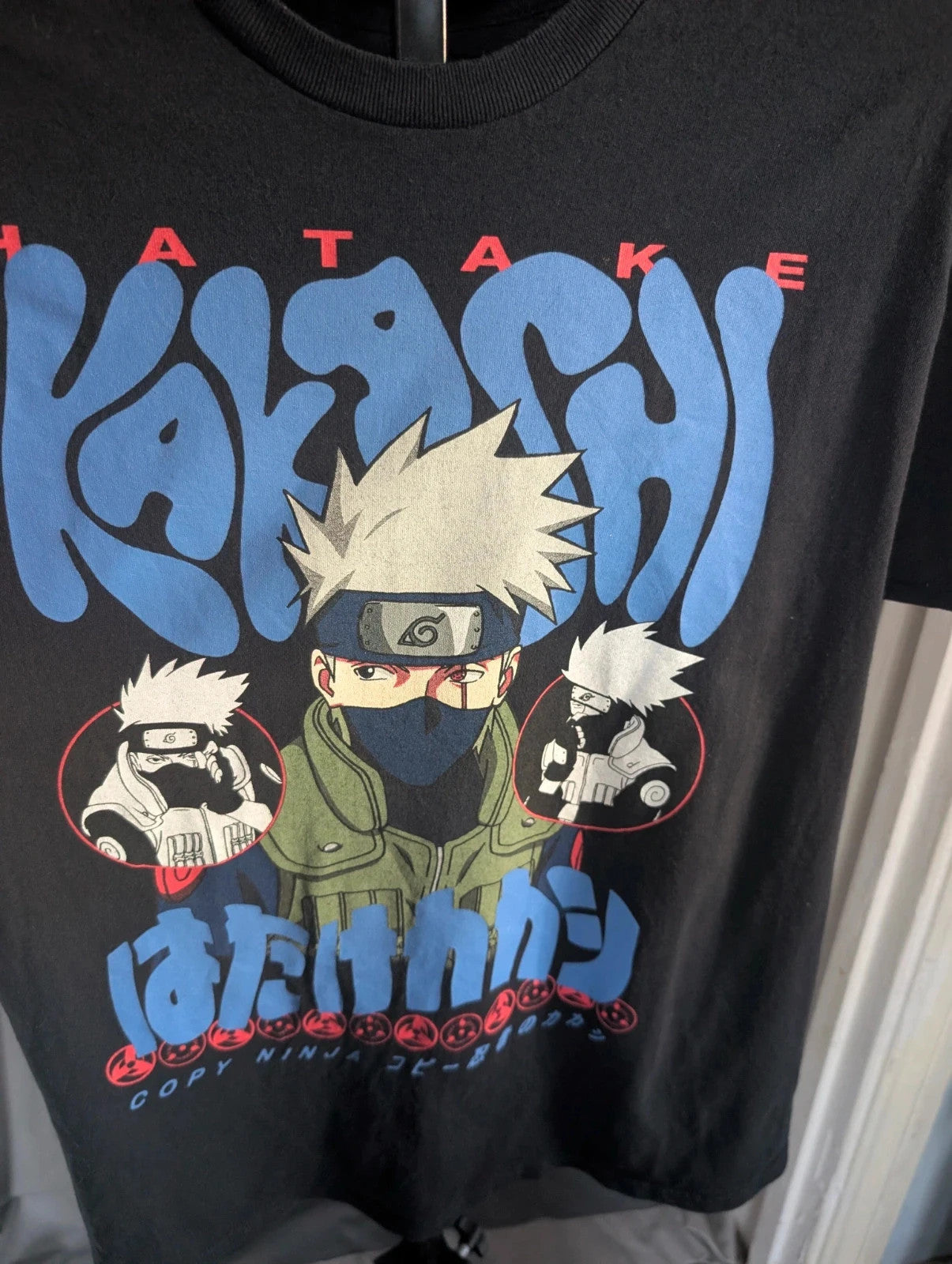 Naruto black graphic t-shirt featuring Kakashi Hatake, bubble typography, and Sharingan eye design.