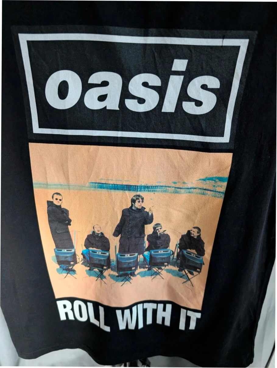 Stanley/Stella black graphic tee featuring Oasis logo and "Roll With It" beach print.
