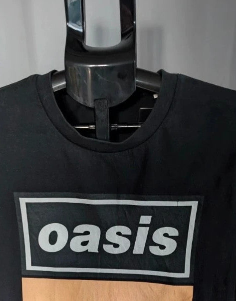 Stanley/Stella black graphic tee featuring Oasis logo and "Roll With It" beach print.