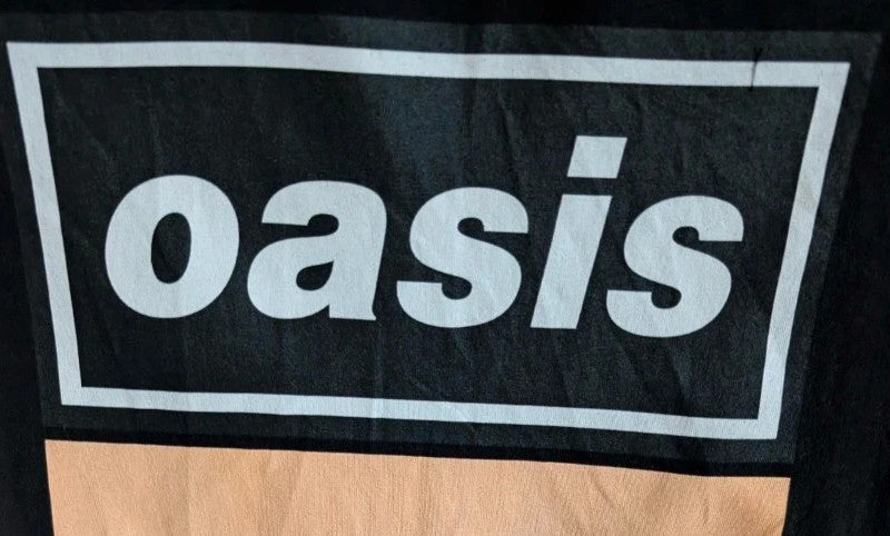 Stanley/Stella black graphic tee featuring Oasis logo and "Roll With It" beach print.